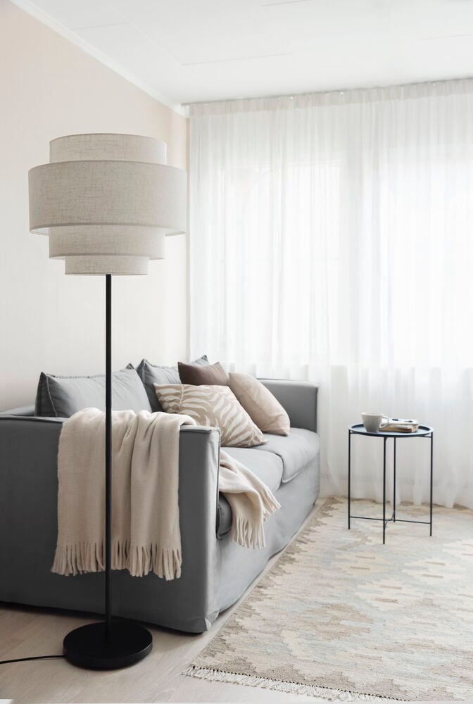 Stor golvlampa med linneskärm i vardagsrum.