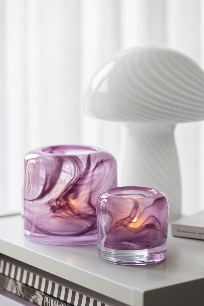 Två lila glasljushållare med struktur på ett bord.