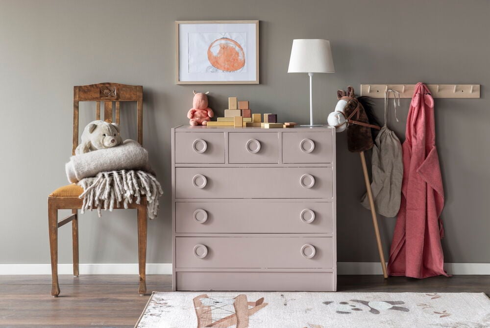 Vaaleanpunainen lipasto pyöristetyillä nupilla harmaata seinää vasten.