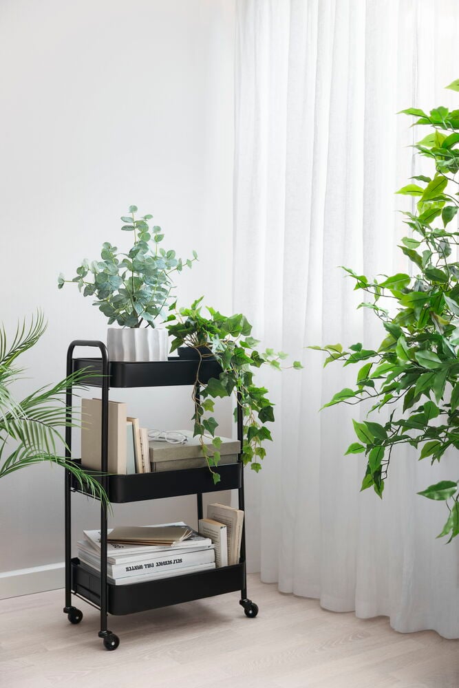 Svart rullvagn med tre hyllor och grön växt.