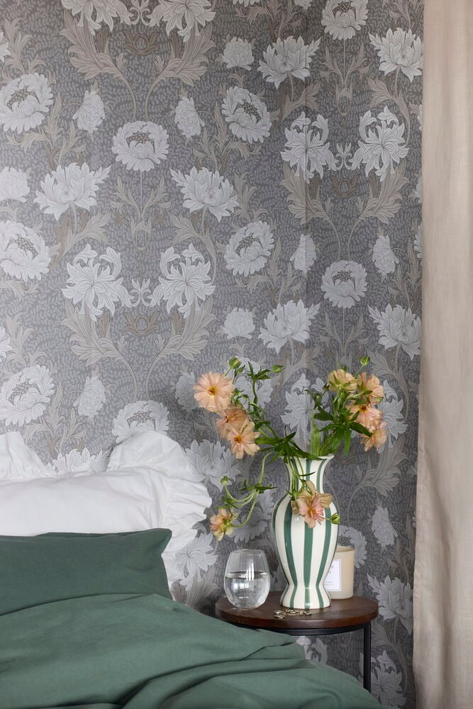 Grå tapet med blommönster bakom säng och bord.