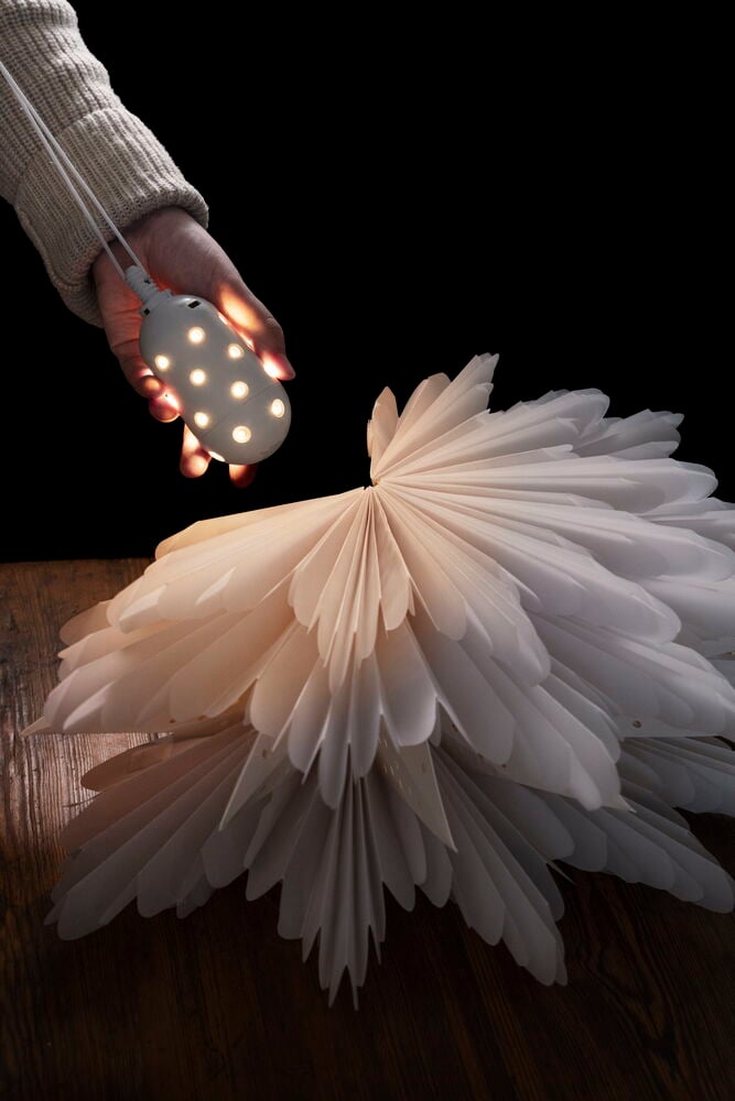 Hand håller uppladdningsbar LED-lampa ovanför vit lampskärm.