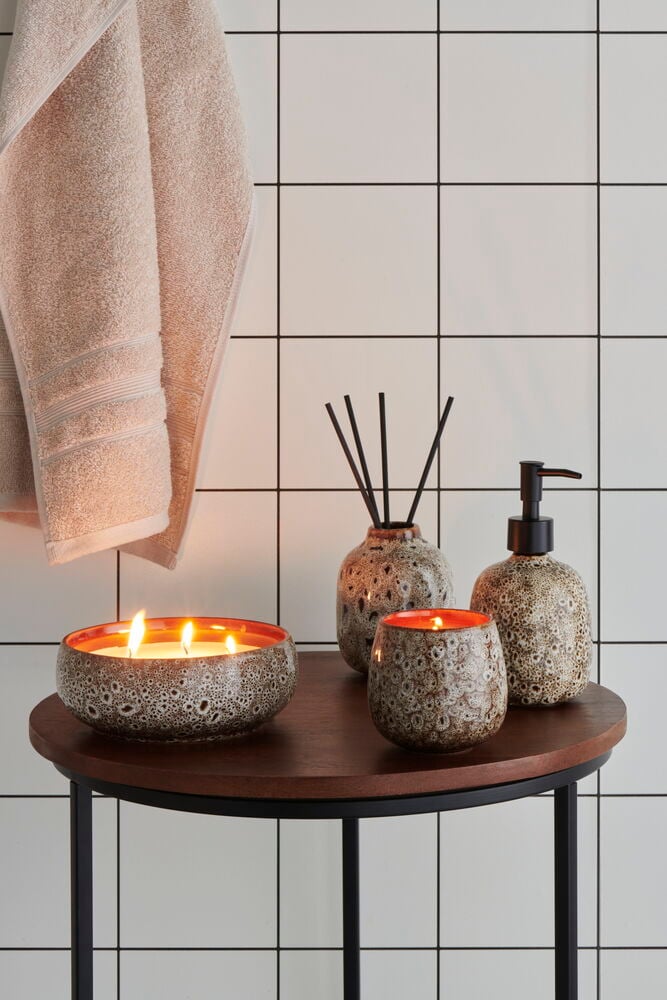 Brunt doftljus på rund träbord i badrum.