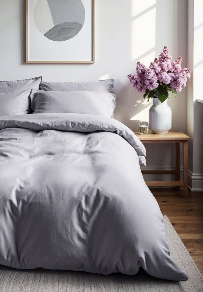 Harmaa polyesterinen pussilakanasetti pedatulla sängyllä.