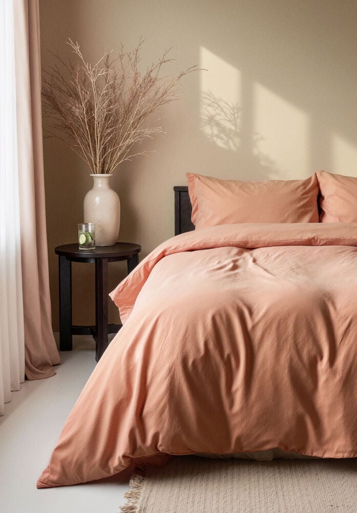 Peittosetti pehmeässä persikanvärissä pedatulla sängyllä.