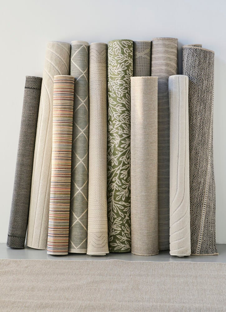 Pystytetyt rullatut matot eri väreissä ja kuvioissa.