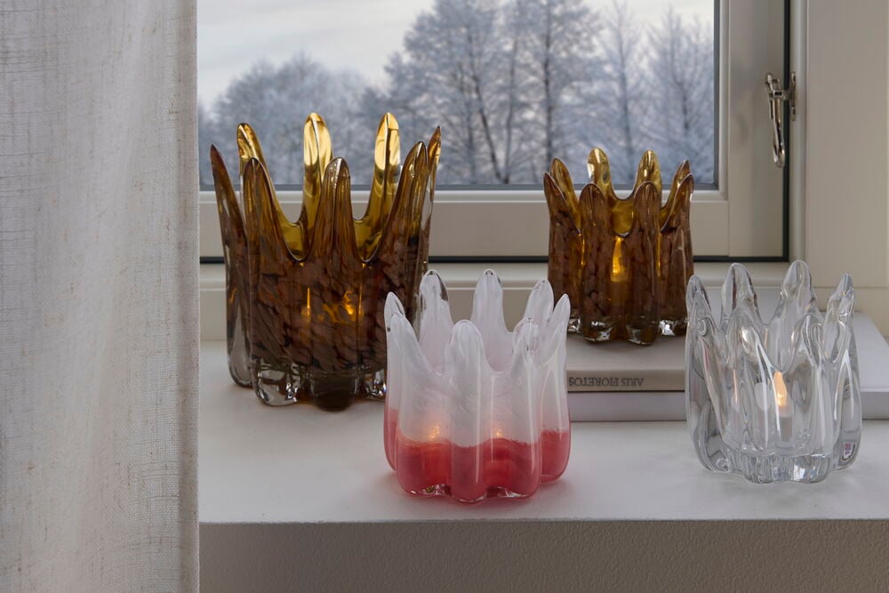 Neljä lasipidikettä tuikkukynttilöille ikkunan luona.