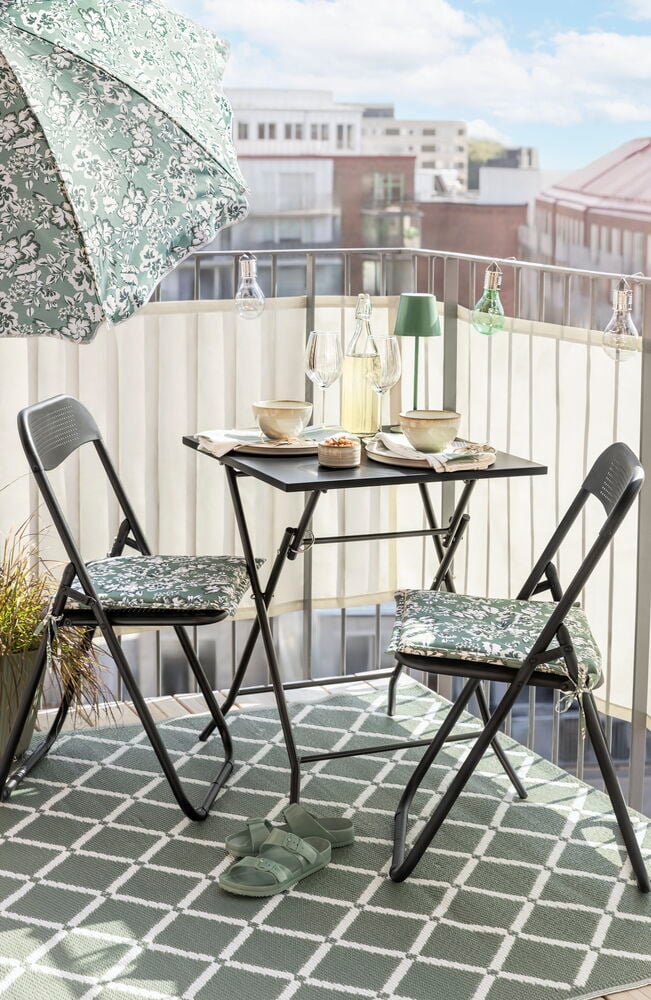 Två svarta fällstolar och bord på balkong.