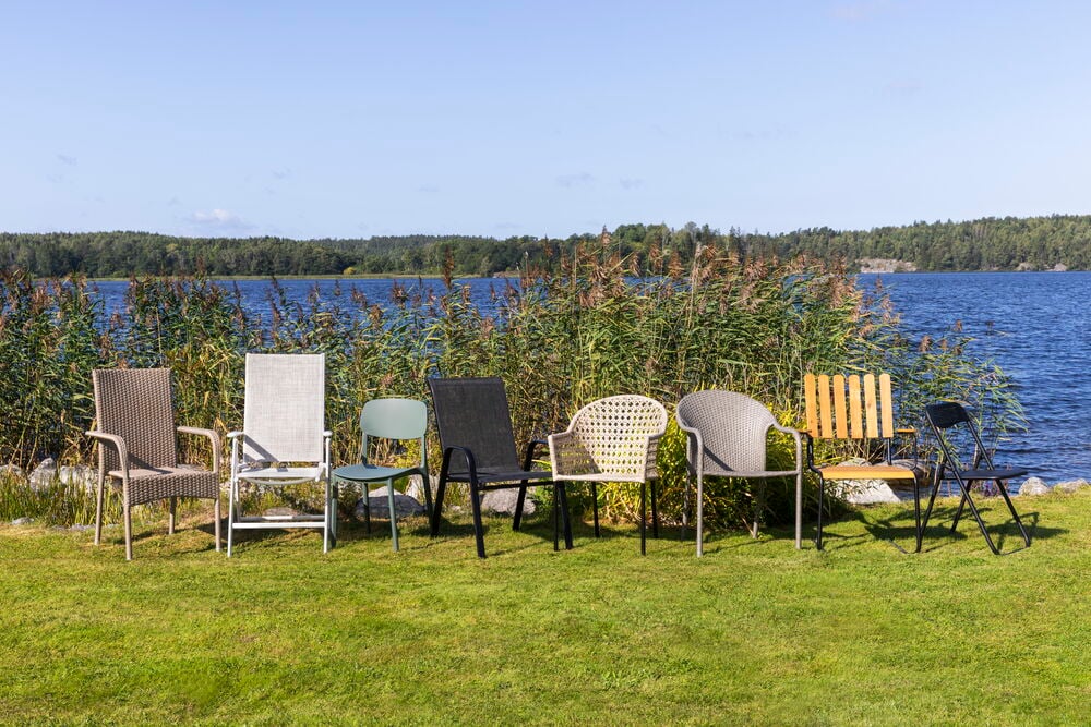 Kuusi ulkotuolia riveissä nurmikolla järven rannalla.