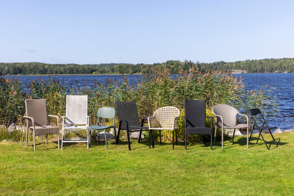 Flera utestolar i olika färger på gräsmatta vid sjö.
