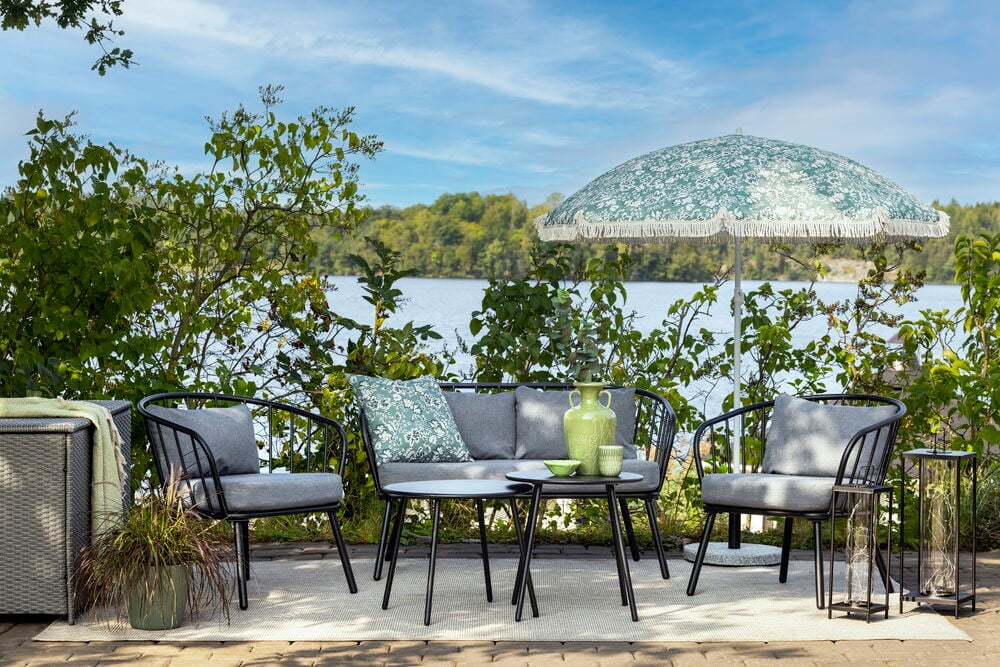 Harmaa keramiikkamaljakko mustalla ulkopöydällä, jossa istuinryhmä.