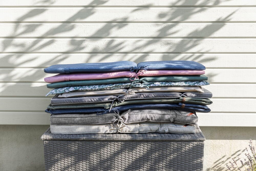 Useita päällekkäin asetettuja puutarhatyynyjä eri väreissä ulkona.