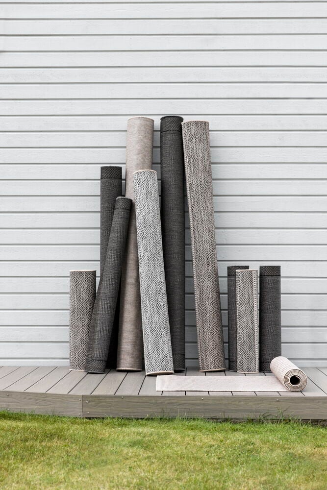 Flera grå mattor upprullade mot vit trävägg.