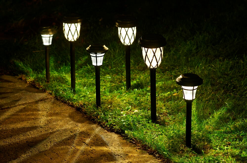 Seks svarte solcellebelysninger lyser opp gress og gangvei.