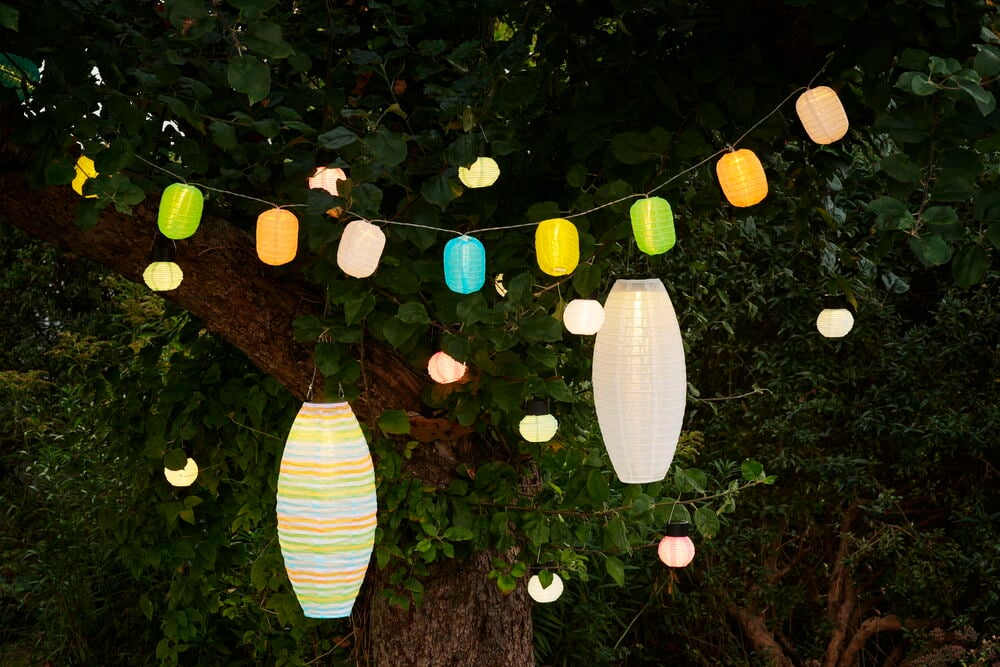 Flera hängande solcellslampor i olika pastellfärger utomhus.