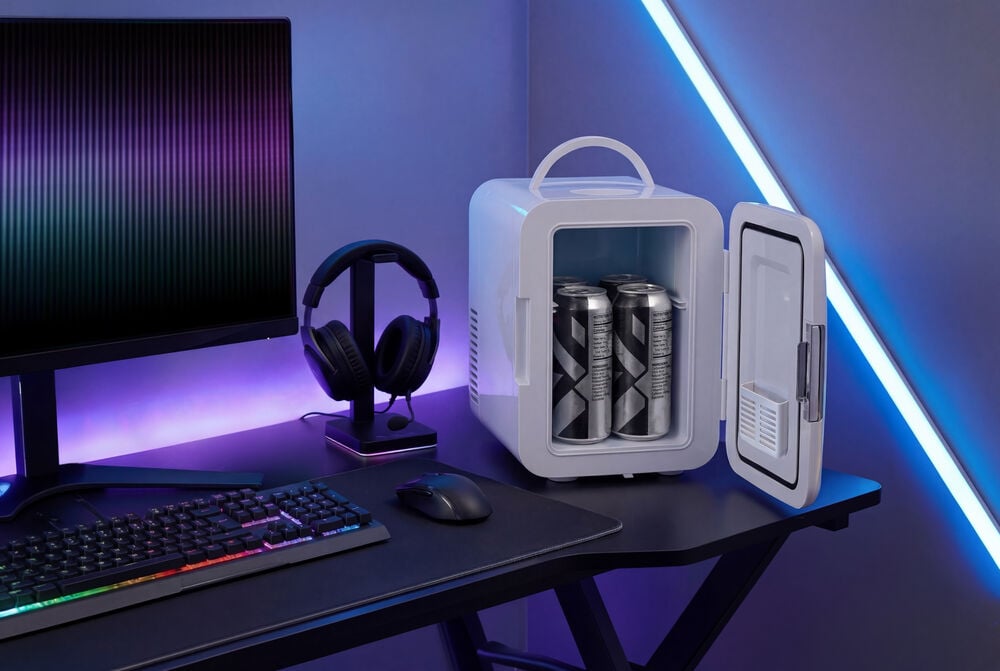 Weißer Mini-Kühlschrank 4 Liter FR26 offen mit Dosen, neben Monitor, Kopfhörern, RGB-Tastatur und Maus.