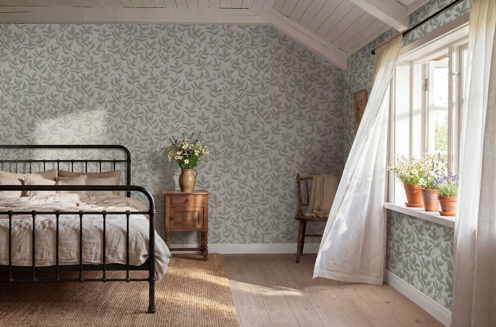 Grön non-woven tapet med grenverksmönster täcker väggarna i ett sovrum.