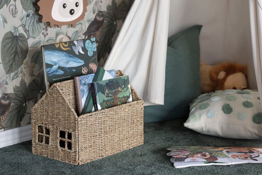 Luonnonvärinen punottu talomallinen Säilytyskori Elsaform Kids 36x22x28 cm House täynnä lastenkirjoja vihreällä matolla.