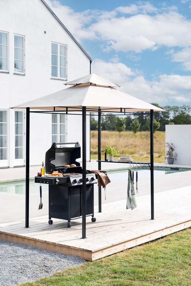 Paviljonki Naxos 2,4x1,5 m vaalealla katolla, tummalla rungolla, peittää mustan kaasugrillin puuterassilla.