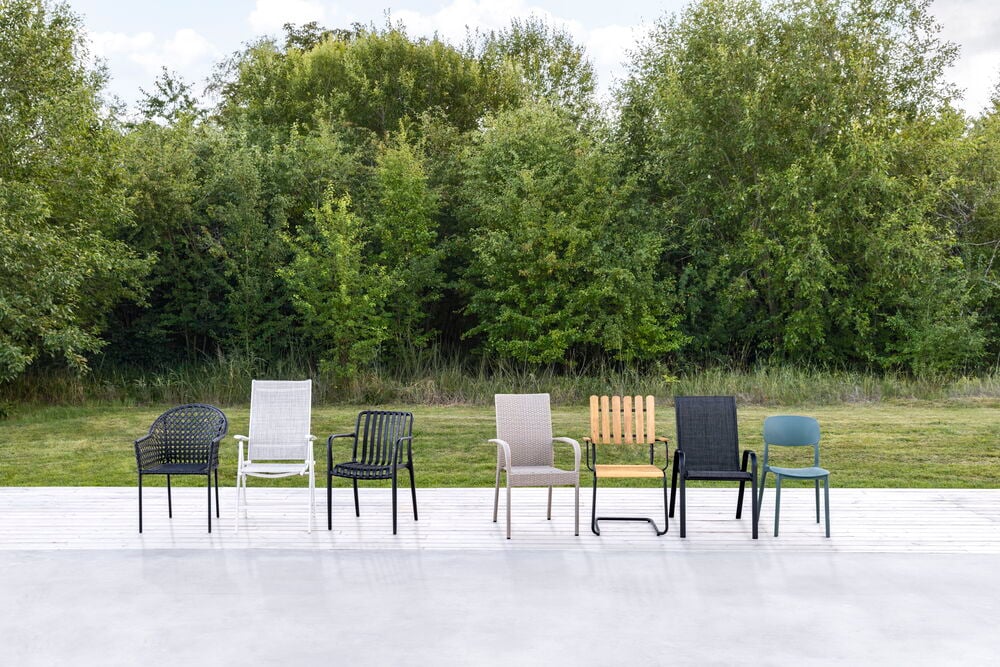 Stuhl Dakar Schwarz und fünf verschiedene Gartenstühle sind auf einer weißen Terrasse im Freien zu sehen.