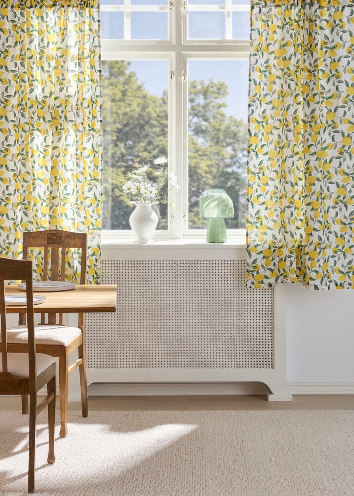 Weiße Vorhänge Cecilia aus recyceltem Polyester mit gelbem Zitronenmuster umrahmen ein Fenster.