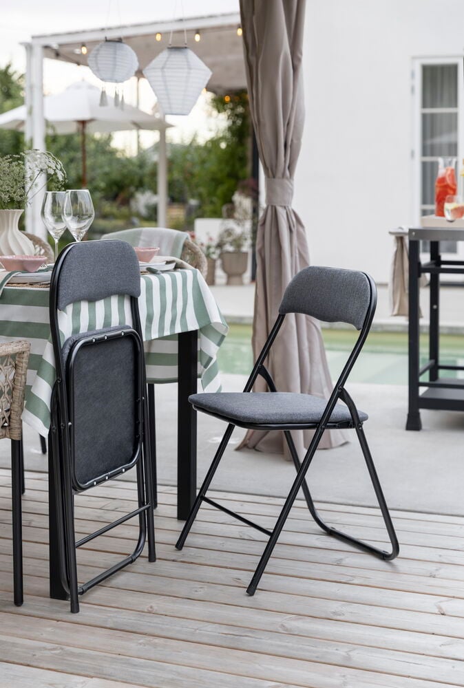 Grå polyester klappstol med vadderad sits, en öppen och en delvis hopfälld, på en trädäck utomhus.