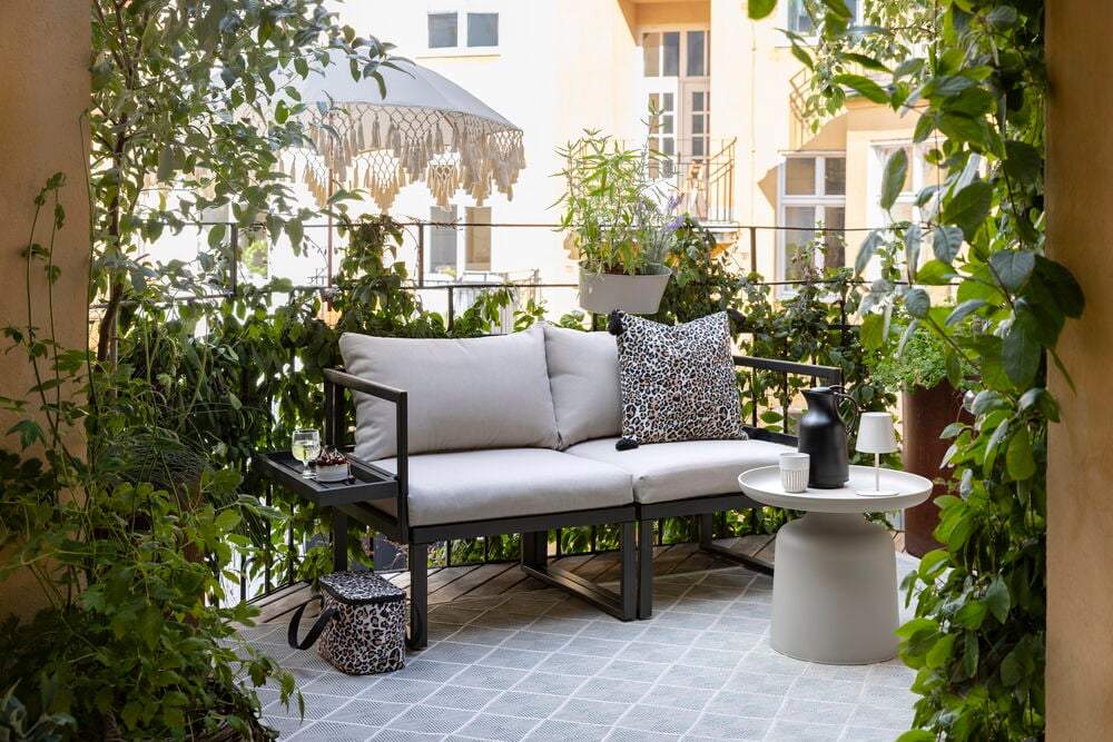 Beistelltisch Tunis Beige, ein beiges Outdoor-Sofa, Leopardenmuster-Kissen und ein gemusterter Teppich.