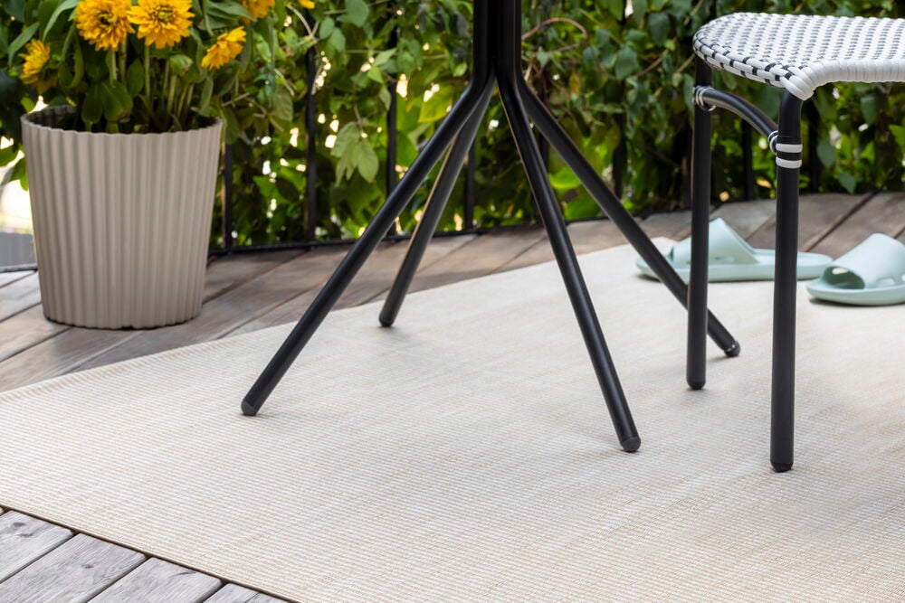Beige polypropen Bastteppe Rihanna med vevd mønster på treterrasse med svarte utemøbler.