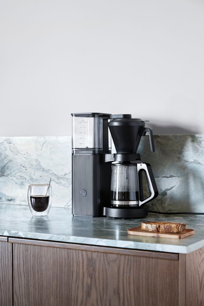 Eine schwarze Kaffeemaschine Excellence CME26 mit Glaskanne, einer Tasse Kaffee und Toast auf einem Brett.