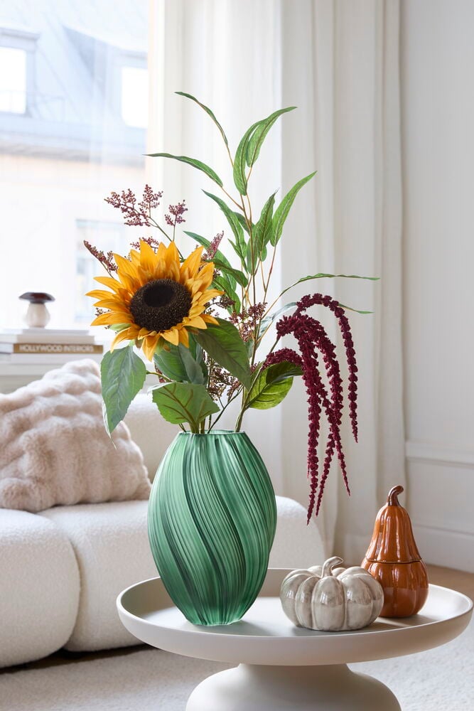 Grüne Vase Selma 27 cm mit gedrehtem Design, enthält einen Sonnenblumenstrauß, neben beiger und oranger Kürbisdeko.
