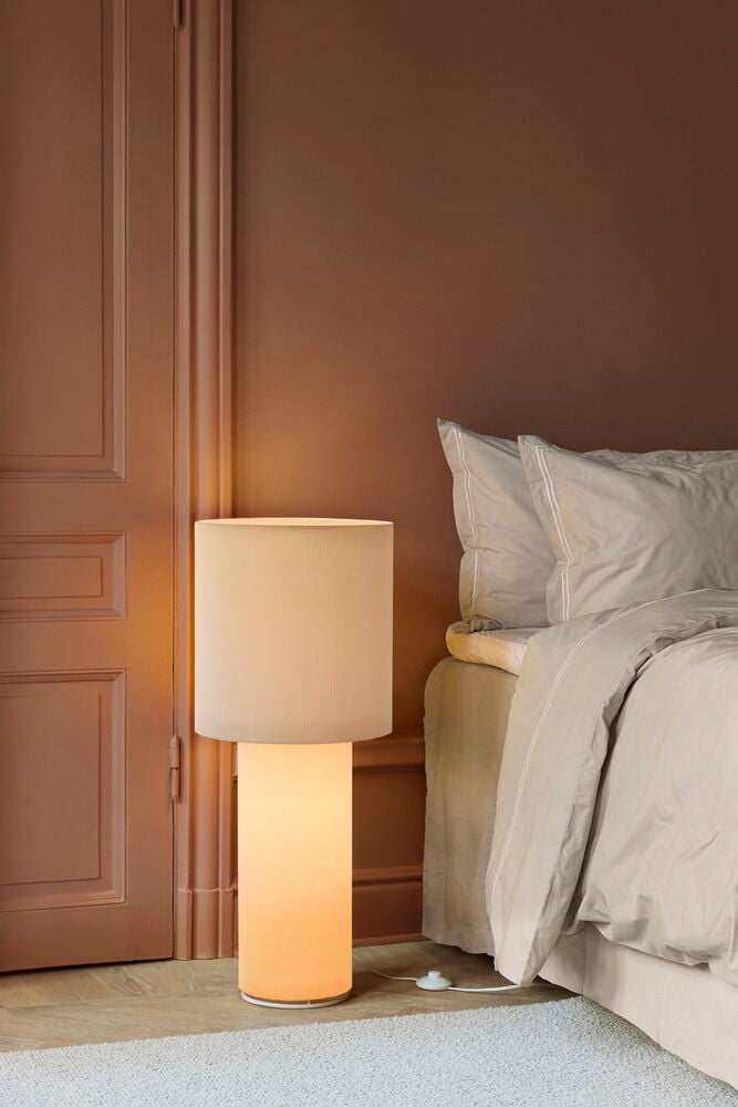 Off-white Fußbodenlampe Porto 37x89 cm, zylindrisch, steht neben einem Bett mit heller Bettwäsche.