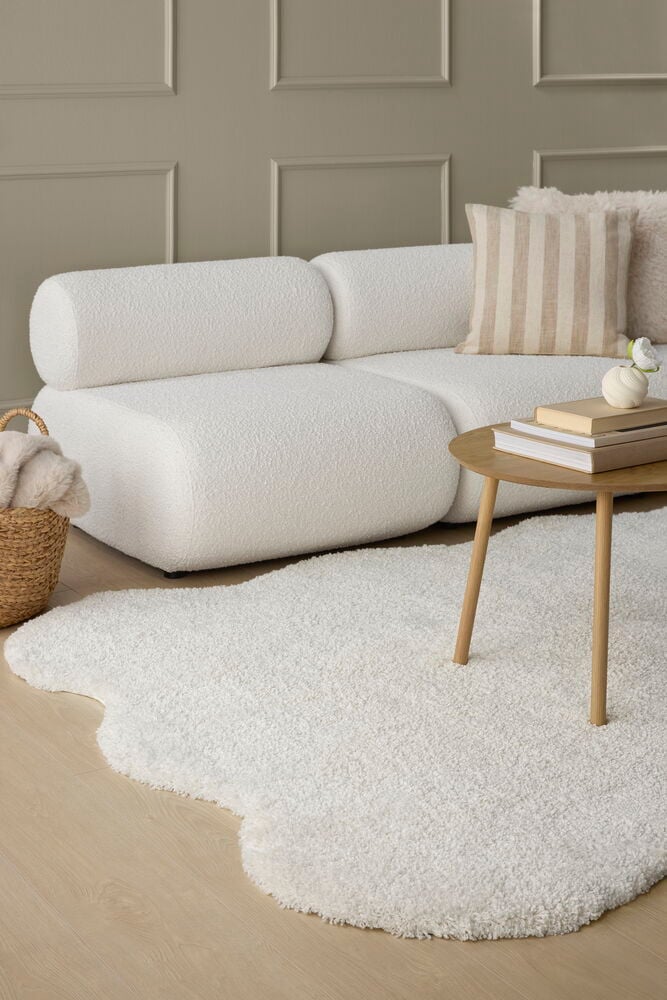 Wandfarbe Nyans Perfect Greige an einer Wand, mit weißem Sofa, gestreiftem Kissen und weißem Teppich.