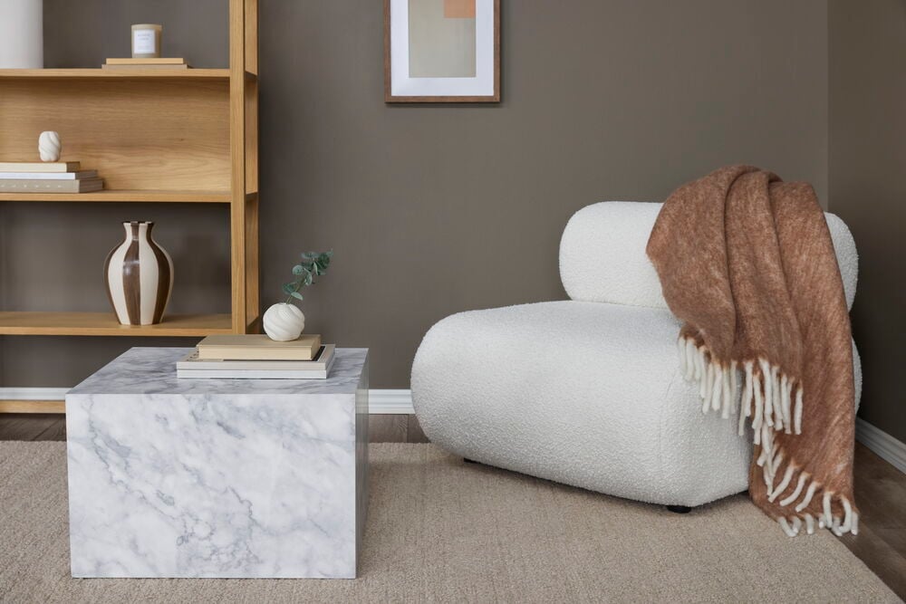 Ein Raum mit einer Wand in dunkelbrauner Wild Truffle Wandfarbe, mit Holzregal, Marmortisch und weißem Sessel.