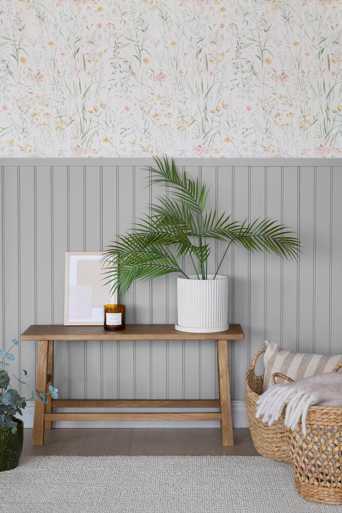 Tapet Boutique Free Flower Cream, lyst blomstermønster over grå panel, med trebenk som holder en grønn plante.