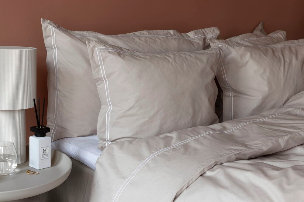 Beige Baumwoll-Kopfkissenbezüge und Bettbezug der Hotel Collection mit weißer Paspel, neben einem weißen Diffusor.