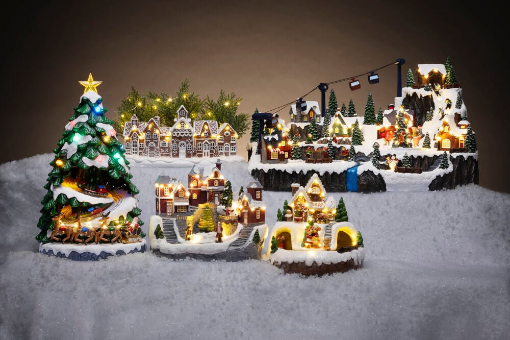 Weihnachtsdorf Ramberg Warmweiß Batteriebetrieben mit Timer zeigt mehrere verschneite Szenen mit beleuchteten Häusern, Baum, Zug und Skilift.