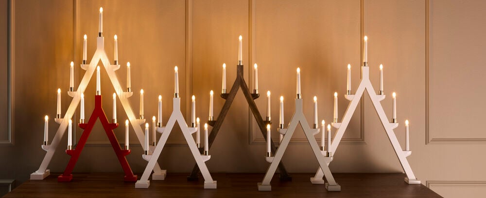Ein beiger Adventsleuchter Jularbo mit sieben elektrischen Lichtern, neben roten, weißen und dunkelbraunen Versionen.