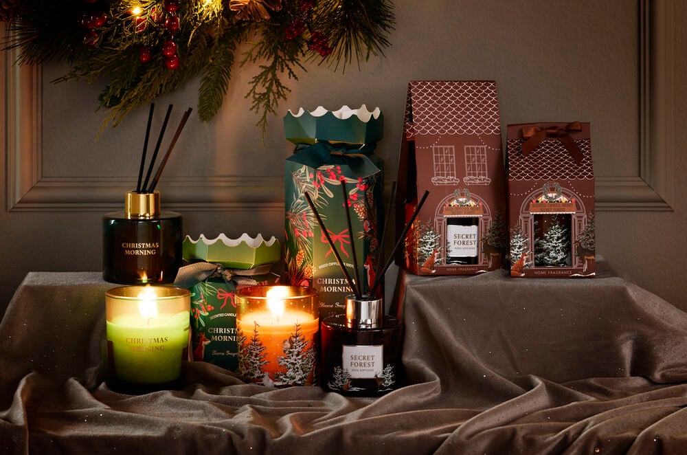 Doftljus Merry med tallträd, grönt ljus, mörka doftspridare och festliga hus- & smällkaramell-presentförpackningar.