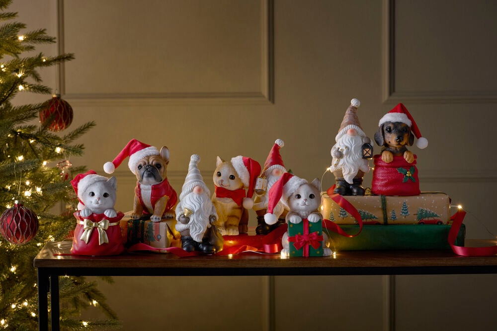 Tre festliga kattfigurer med tomteluva, några i presentpåsar, visas med hund- och tomtedekorationer.
