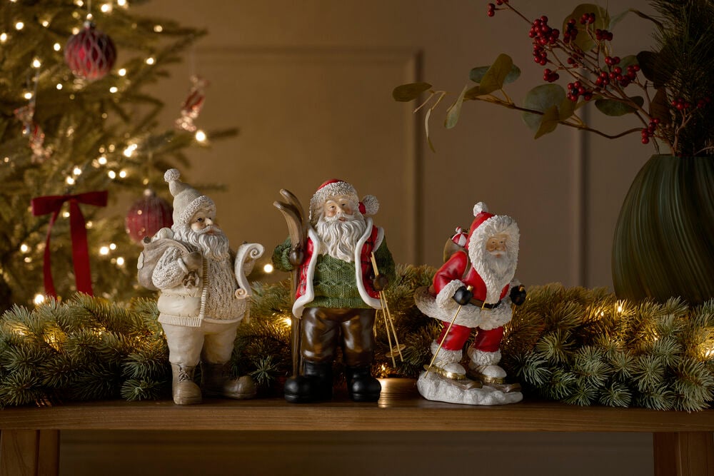 Dekoration Weihnachtsmann 25 cm Beige Figur mit Sack, Rolle, Mütze, Mantel; daneben zwei skifahrende Weihnachtsmänner.