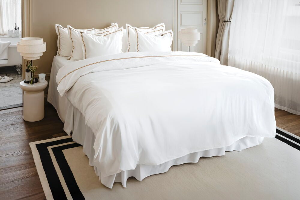 Hvit bomullsputevar Hotel Collection 50x90 cm med gullkant, med matchende dynetrekk på en seng.