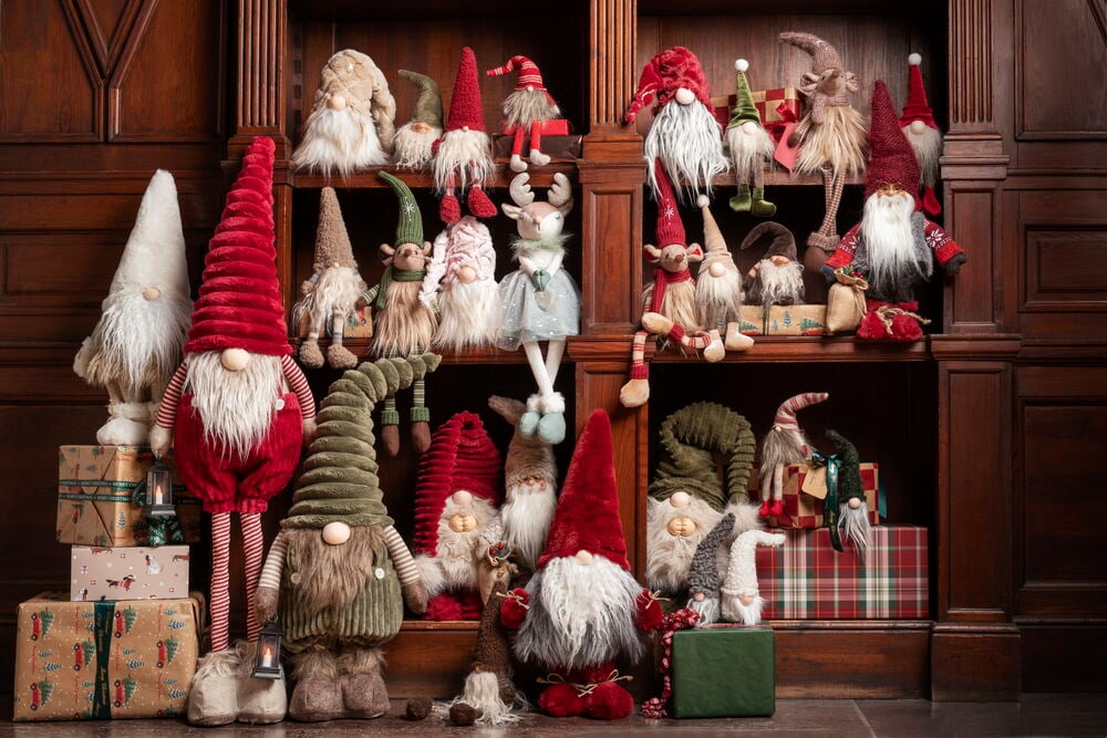 Weihnachtswichtel Vidar, ein großer roter Wichtel mit weißem Bart und gestreiften Beinen, hält eine Laterne, umgeben von Wichteln.