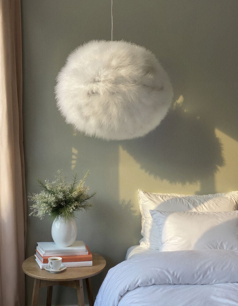 Vit fluffig taklampa ovanför bäddad säng och nattduksbord.