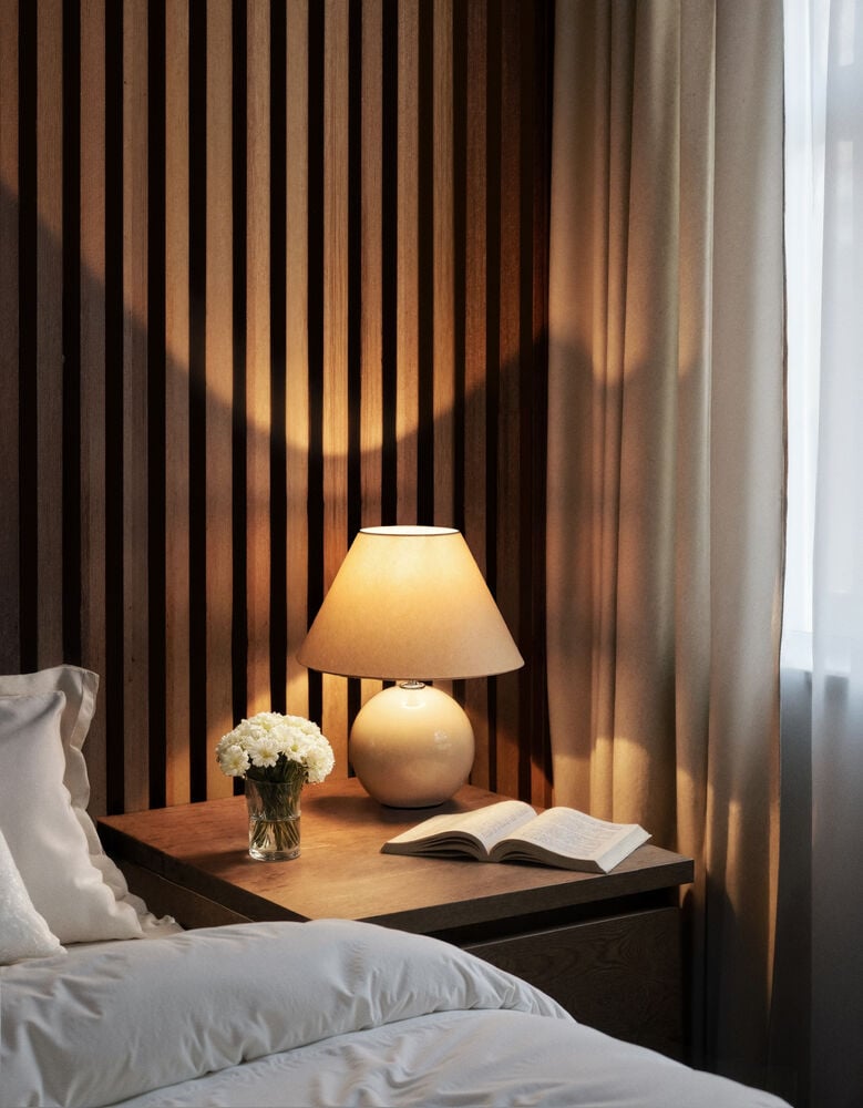 Beige bordslampa på nattduksbord bredvid säng.