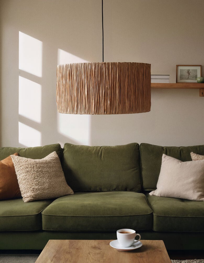 Taklampskärm i naturfärgad raffia över grön soffa.