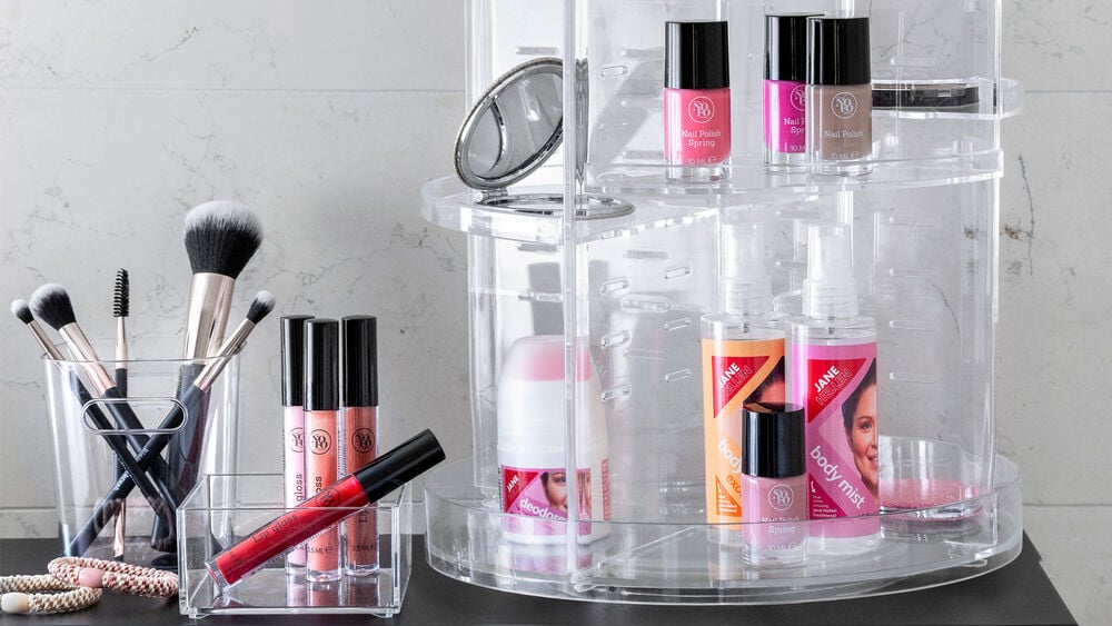 Sminkprodukter och borstar är organiserade i genomskinliga behållare på ett badrumsskåp.