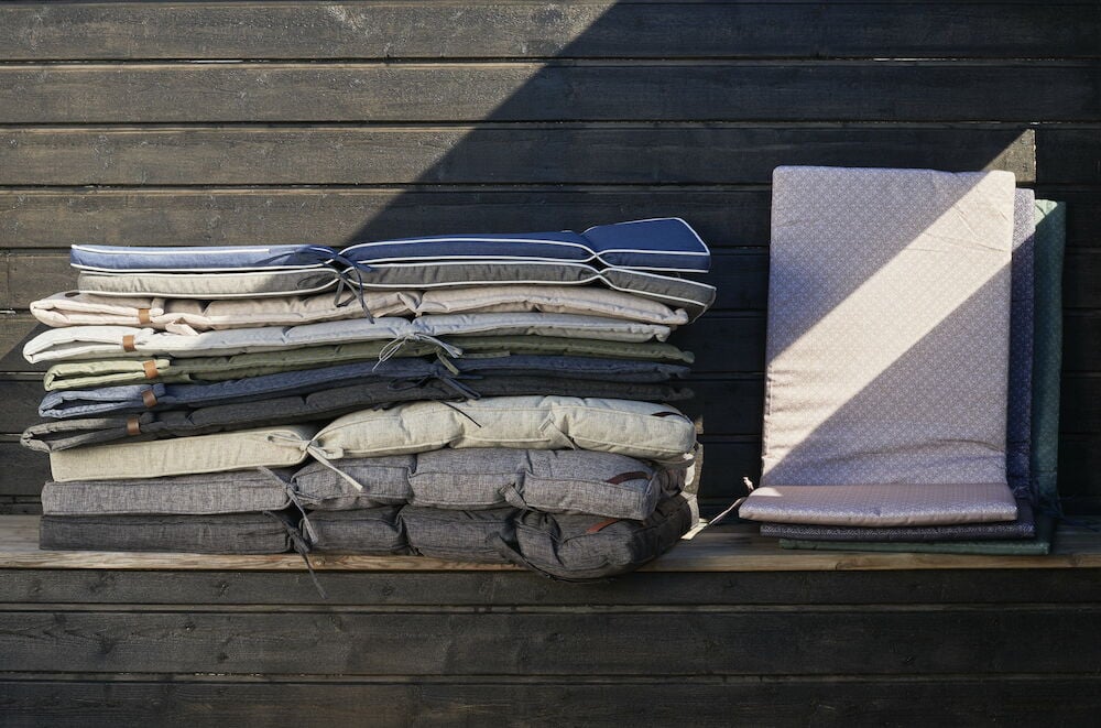 Useita päällekkäin pinottuja ulkotyynyjä tummaa puuseinää vasten.