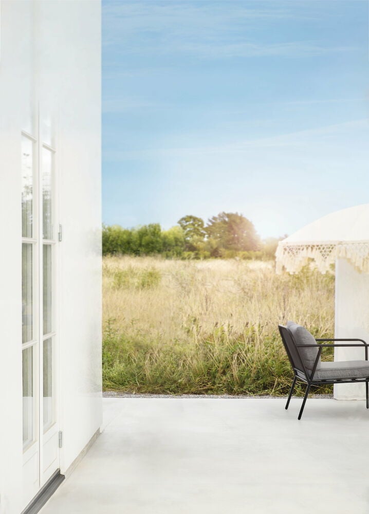 Vitt parasoll med fransar på uteplats vid fält.