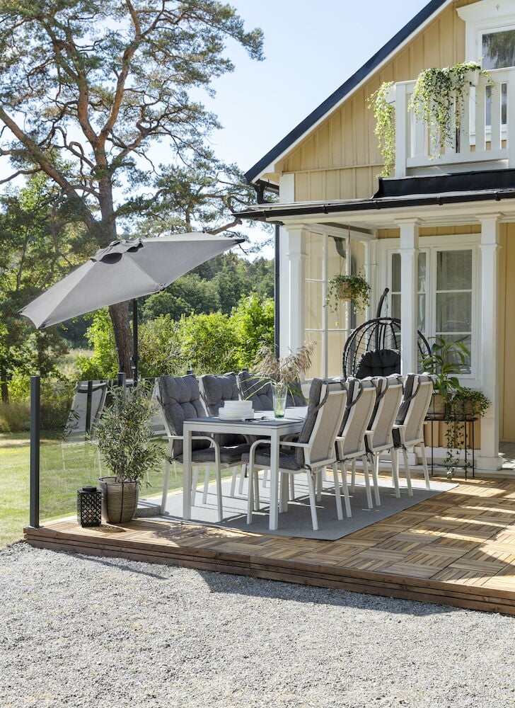 Glasräcke i rökgrått runt altan med matgrupp.