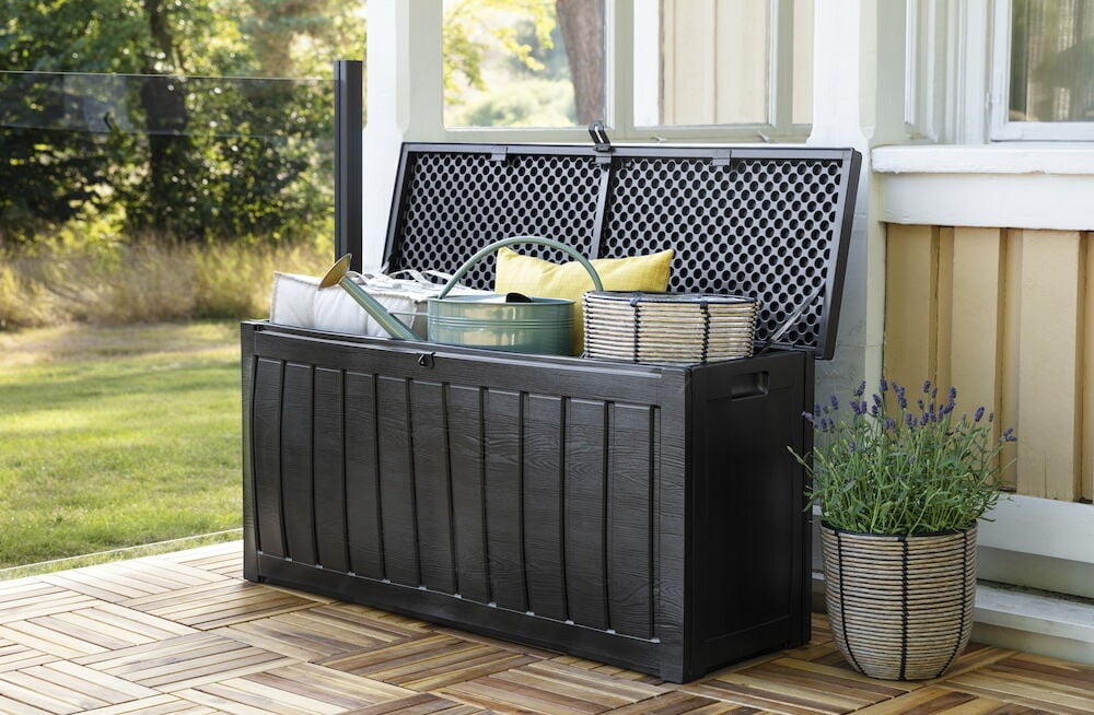 Musta muovilaatikko, jossa avattu kansi ja puutarhatarvikkeita.